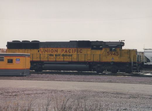 Side view of a yellow and black Union Pacific diesel locomotive numbered 5945, standing in a snow-dusted railyard next to a caboose.