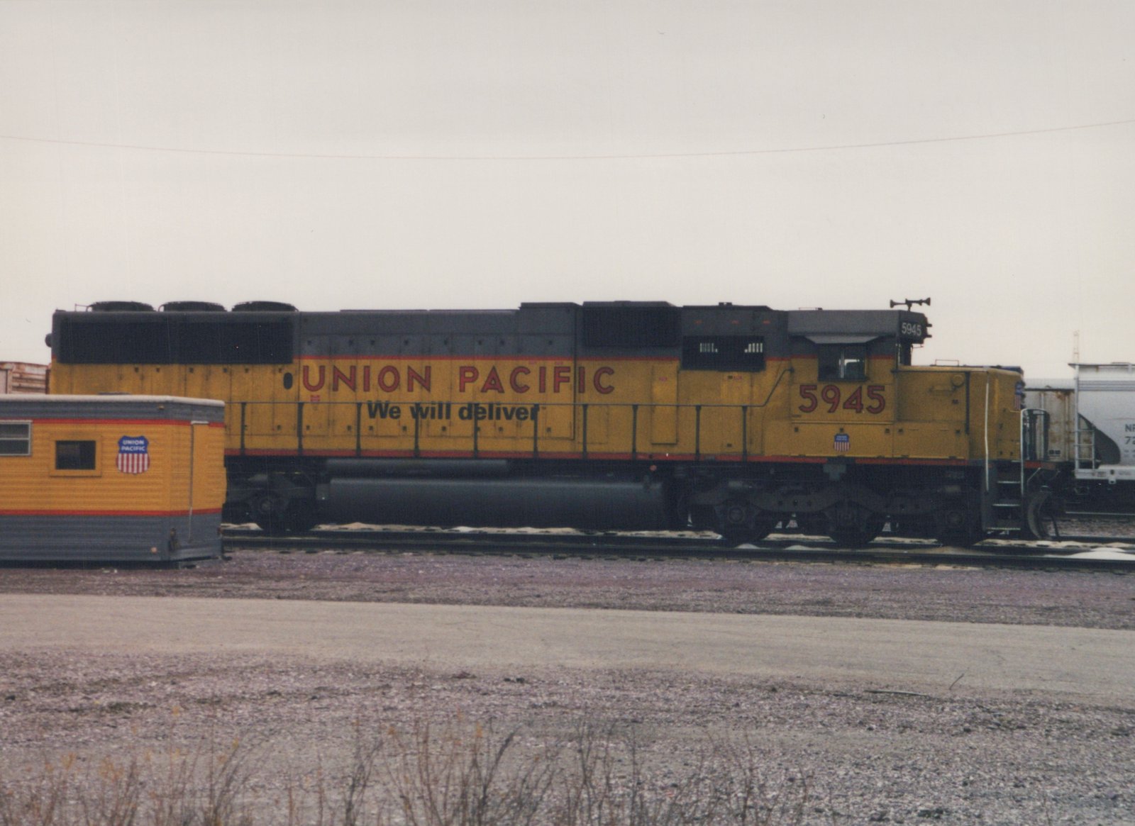 Side view of a yellow and black Union Pacific diesel locomotive numbered 5945, standing in a snow-dusted railyard next to a caboose.