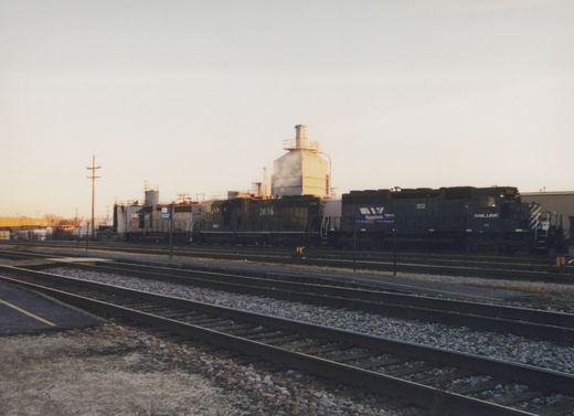 Two diesel locomotives, one blue with 'Rail Link' lettering and number 202, and one dark with number 2036, sit on parallel tracks at a railroad yard at dusk.