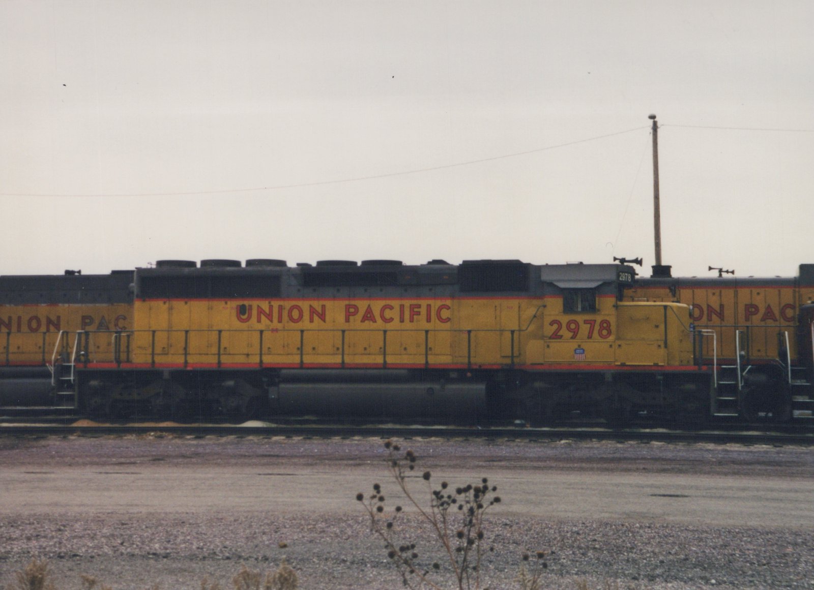 A side view of a yellow and black Union Pacific diesel locomotive numbered 2978, sitting on tracks in a gravel yard under an overcast sky.