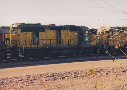 A side view of two yellow and dark green diesel locomotives, number 5535 in front and 1796 behind, in a gravel yard with bare tree branches in the foreground.