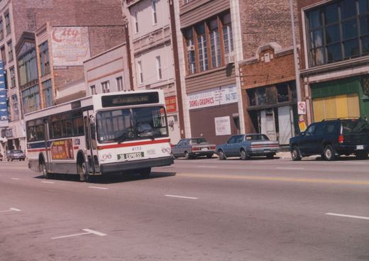 A white and red Chicago Transit Authority bus with the number 4113 and route 38 Express sign travels down a city street lined with brick buildings and parked cars.