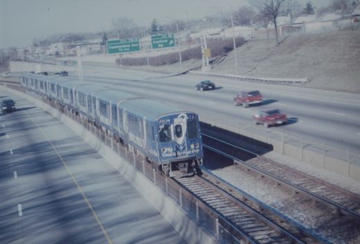 A blue CTA rapid transit train numbered 311 travels on an elevated track next to a highway with cars driving by under a clear winter sky.