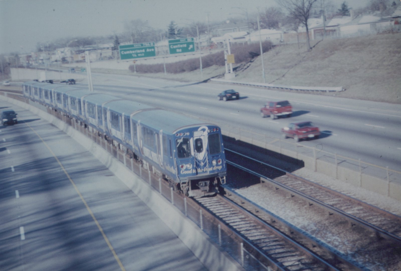 A blue CTA rapid transit train numbered 311 travels on an elevated track next to a highway with cars driving by under a clear winter sky.
