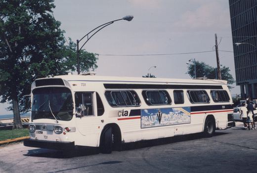 Side view of a white CTA bus with number 731 and a Grand Victoria Casino ad, parked on a street with pedestrians and a tall building in the background.