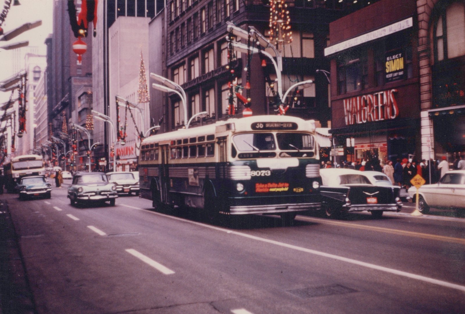 A Chicago Transit Authority trolleybus with the number 8073, running on route 36, is shown on a decorated city street lined with 1950s cars and a Walgreens store.