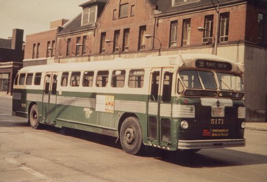 A green and white Chicago Transit Authority motor bus, number 5171, on route 56 Milwaukee-Downtown, parked on a city street in front of a brick building.