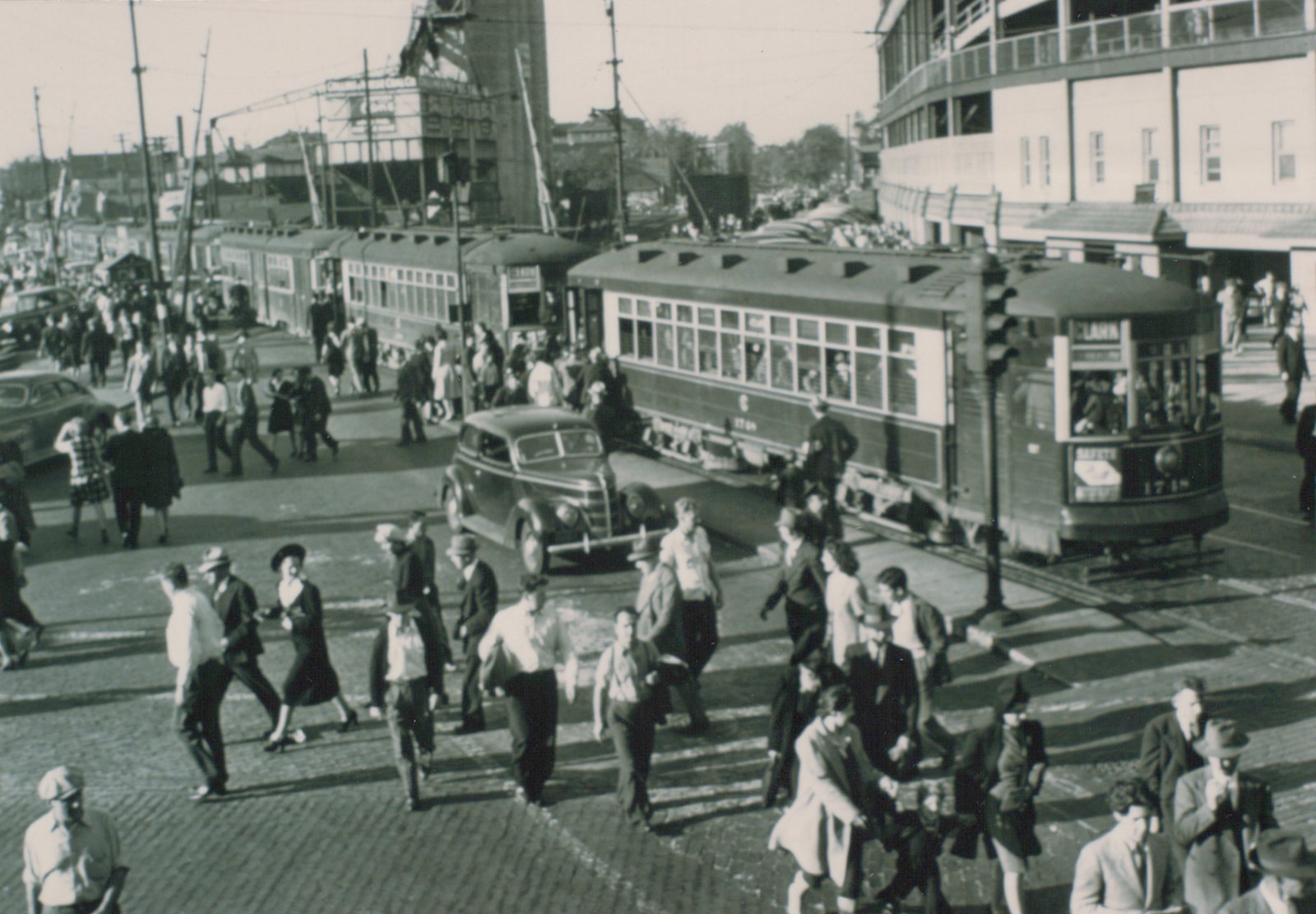 A bustling 1940s street scene in Chicago with two vintage streetcars, many pedestrians, and classic automobiles at the intersection of Clark and Addison, with Wrigley Field visible in the background.