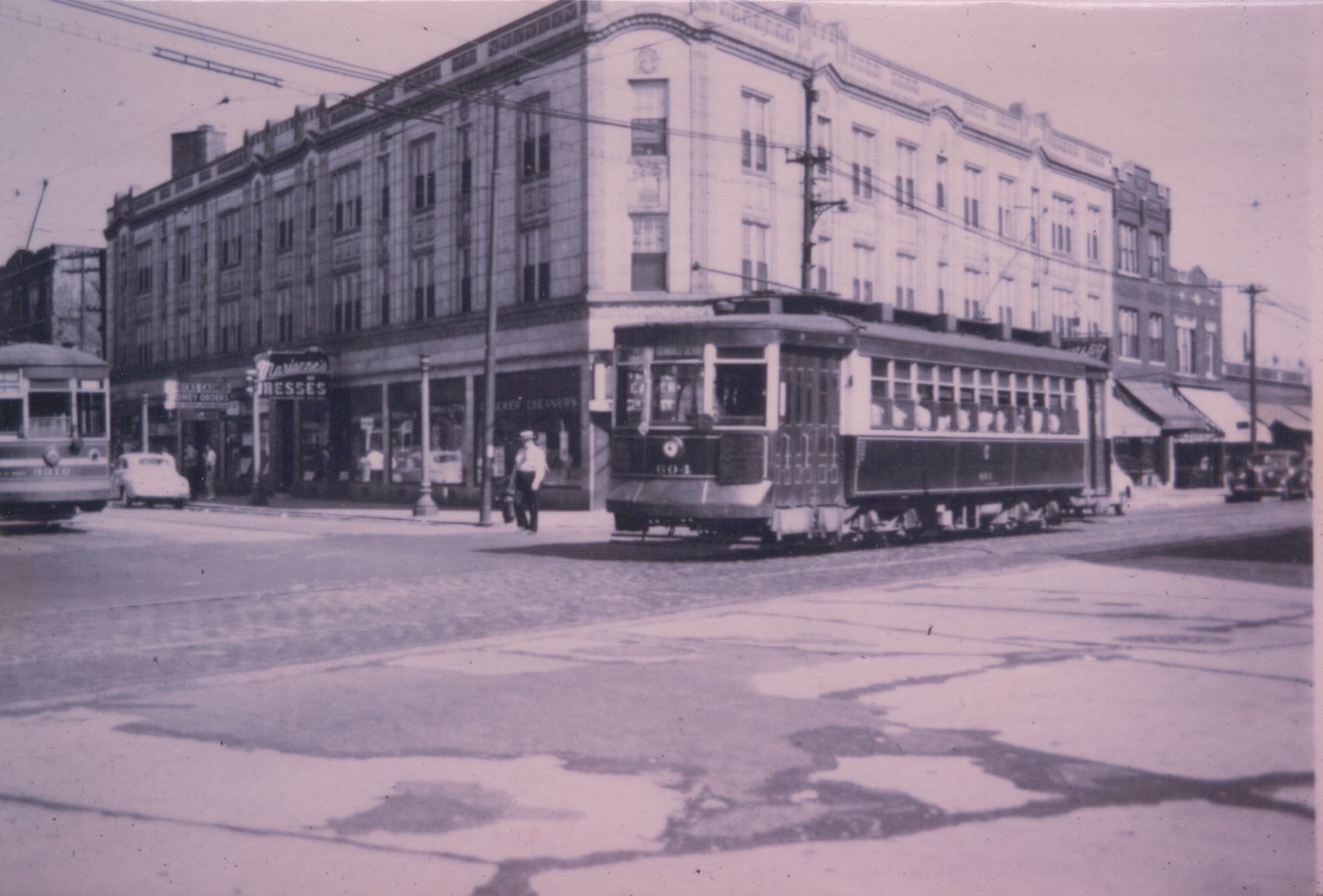 A black and white photo of two vintage streetcars, numbers 604 and 8010, operating on a city street lined with shops and a few automobiles.
