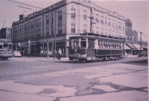A black and white photo of two vintage streetcars, numbers 604 and 8010, operating on a city street lined with shops and a few automobiles.