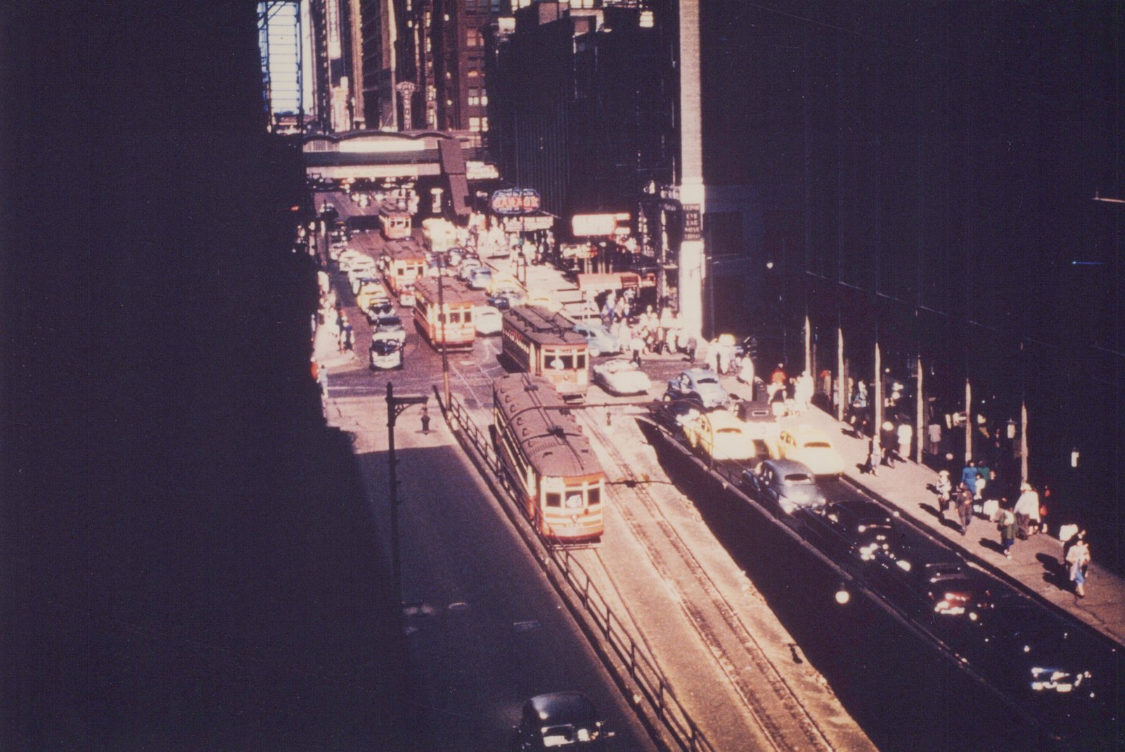High-angle view of a bustling city street with multiple streetcars, cars, and pedestrians under a clear sky.