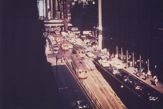 High-angle view of a bustling city street with multiple streetcars, cars, and pedestrians under a clear sky.