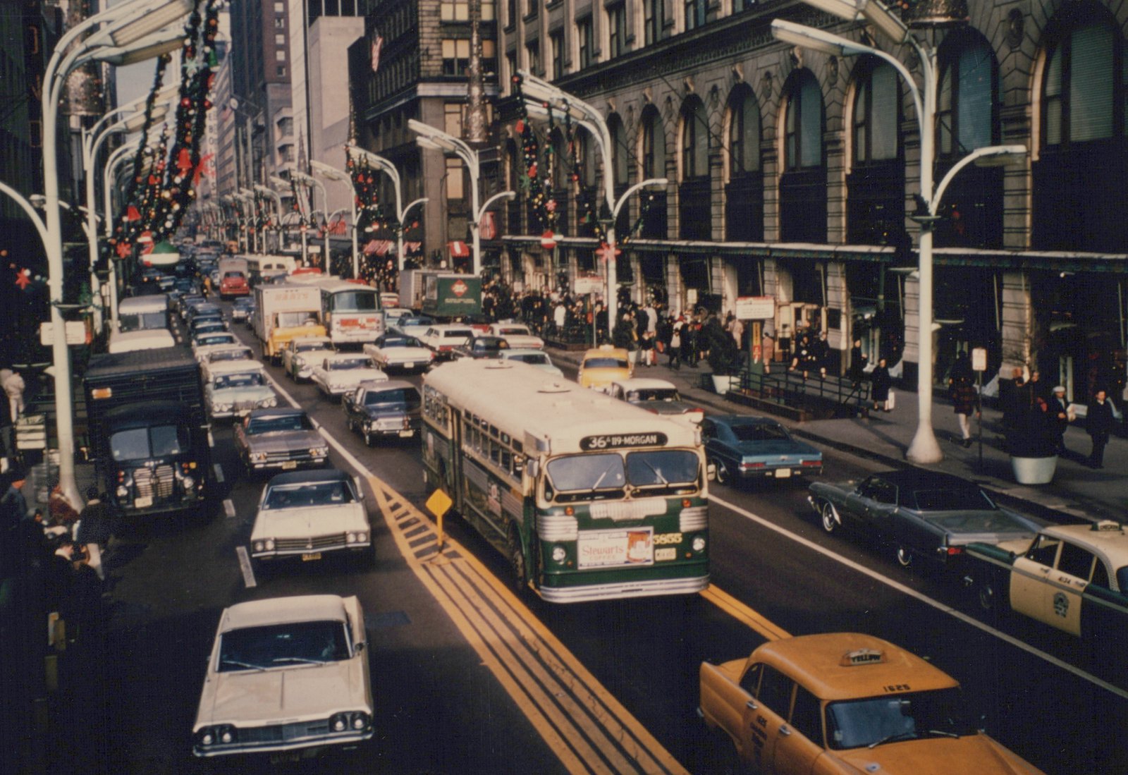 A green and cream CTA bus drives down a busy city street decorated for Christmas, with many cars and people on the sidewalks.
