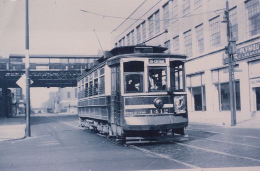 A vintage black and white photo of a Chicago streetcar, number 1412, on the 26-Cottage route, driving on a street with an elevated train track in the background and a building labeled 'PLYMOUTH' on the right.