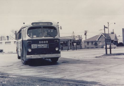 Front view of a dark-colored CTA bus with the number 2603 and route 49 A Western-79 displayed, stopped at an intersection with a stop sign and a street sign for W 119th St visible.