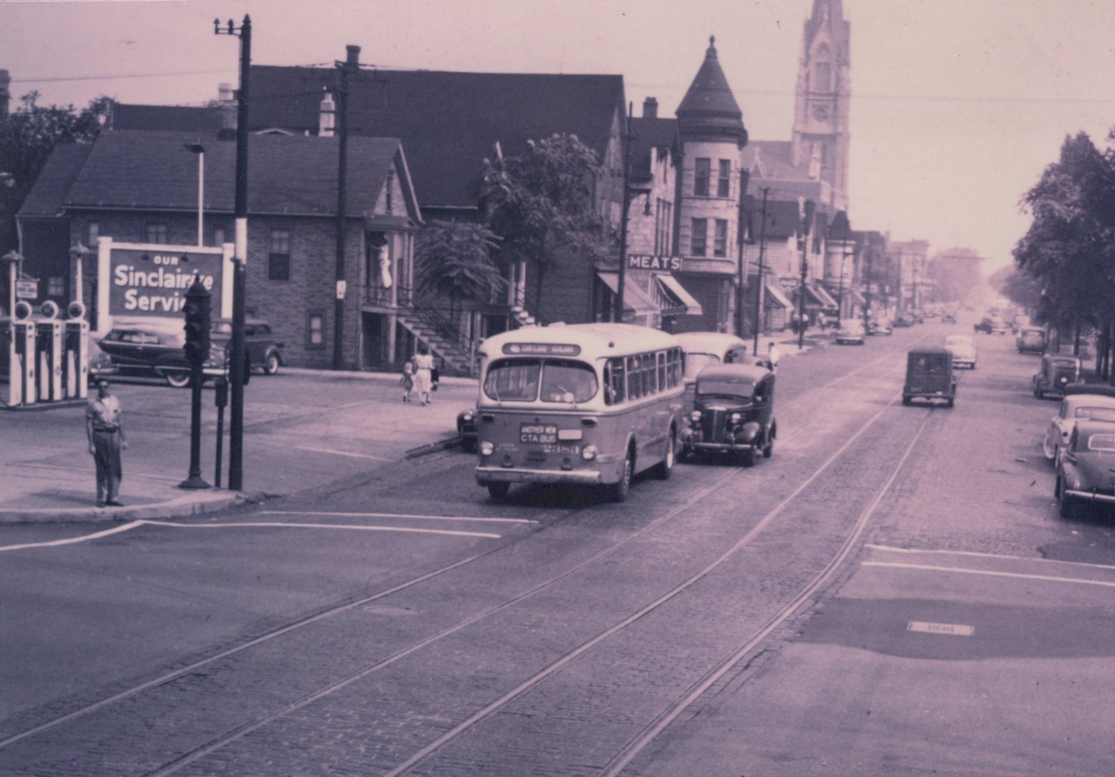 A vintage black-and-white photograph of a Chicago Transit Authority bus from the 1950s on a city street, with embedded trolley tracks, classic cars, and a Sinclair gas station in the background.