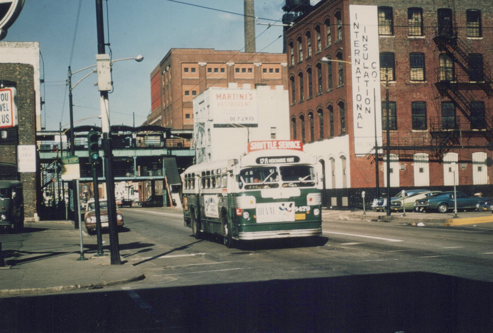A green and cream Chicago Transit Authority bus, number 3429, drives down a city street with an elevated structure and brick buildings in the background.