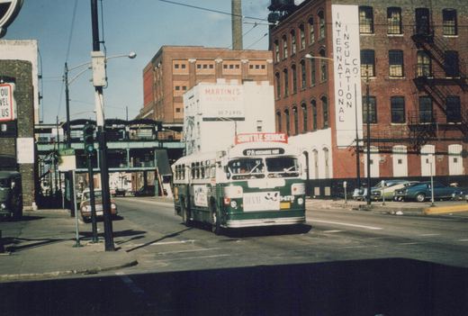 A green and cream Chicago Transit Authority bus, number 3429, drives down a city street with an elevated structure and brick buildings in the background.