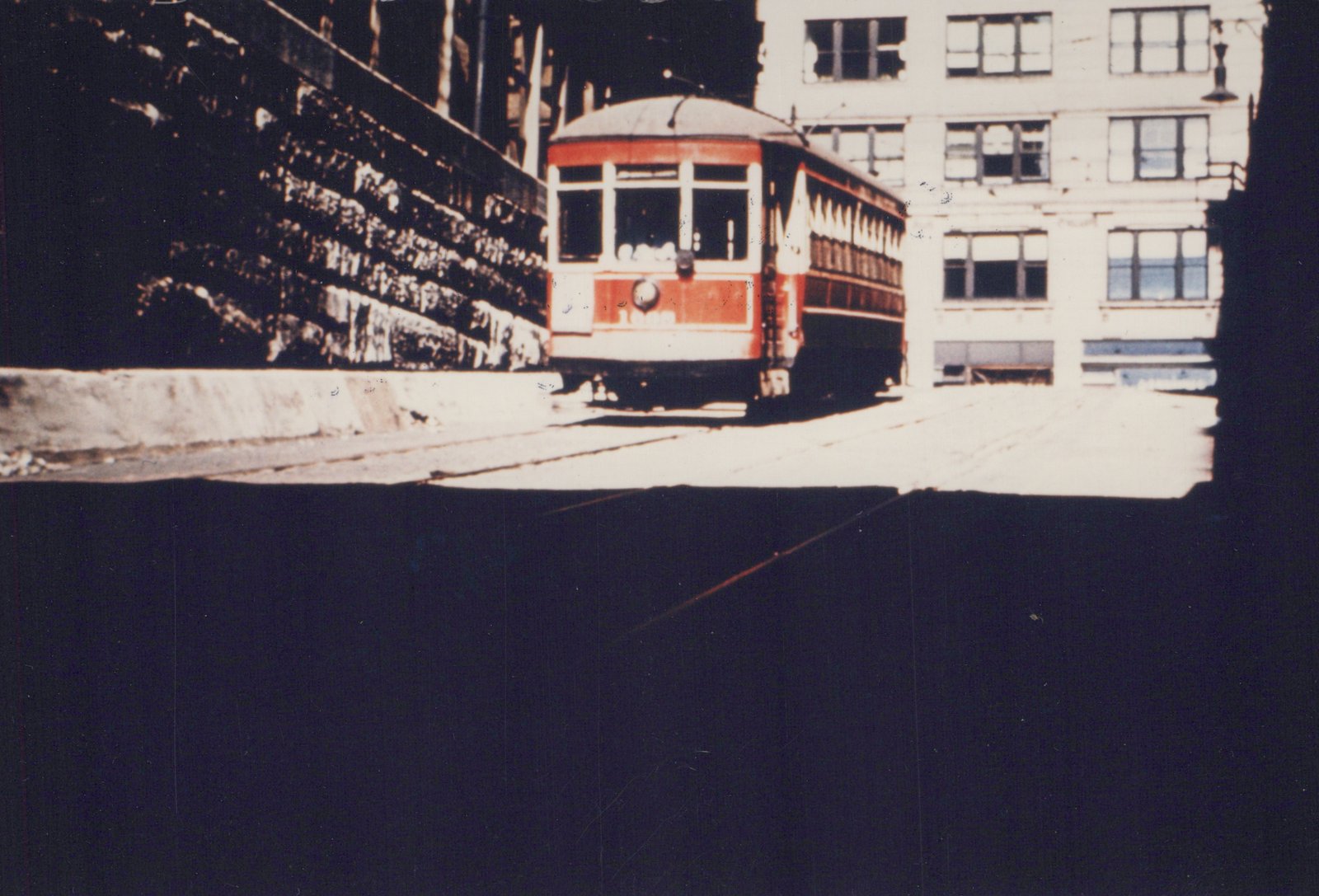 A red and cream streetcar, number 1693, is shown on a city street in front of a building, with tracks visible on the ground.