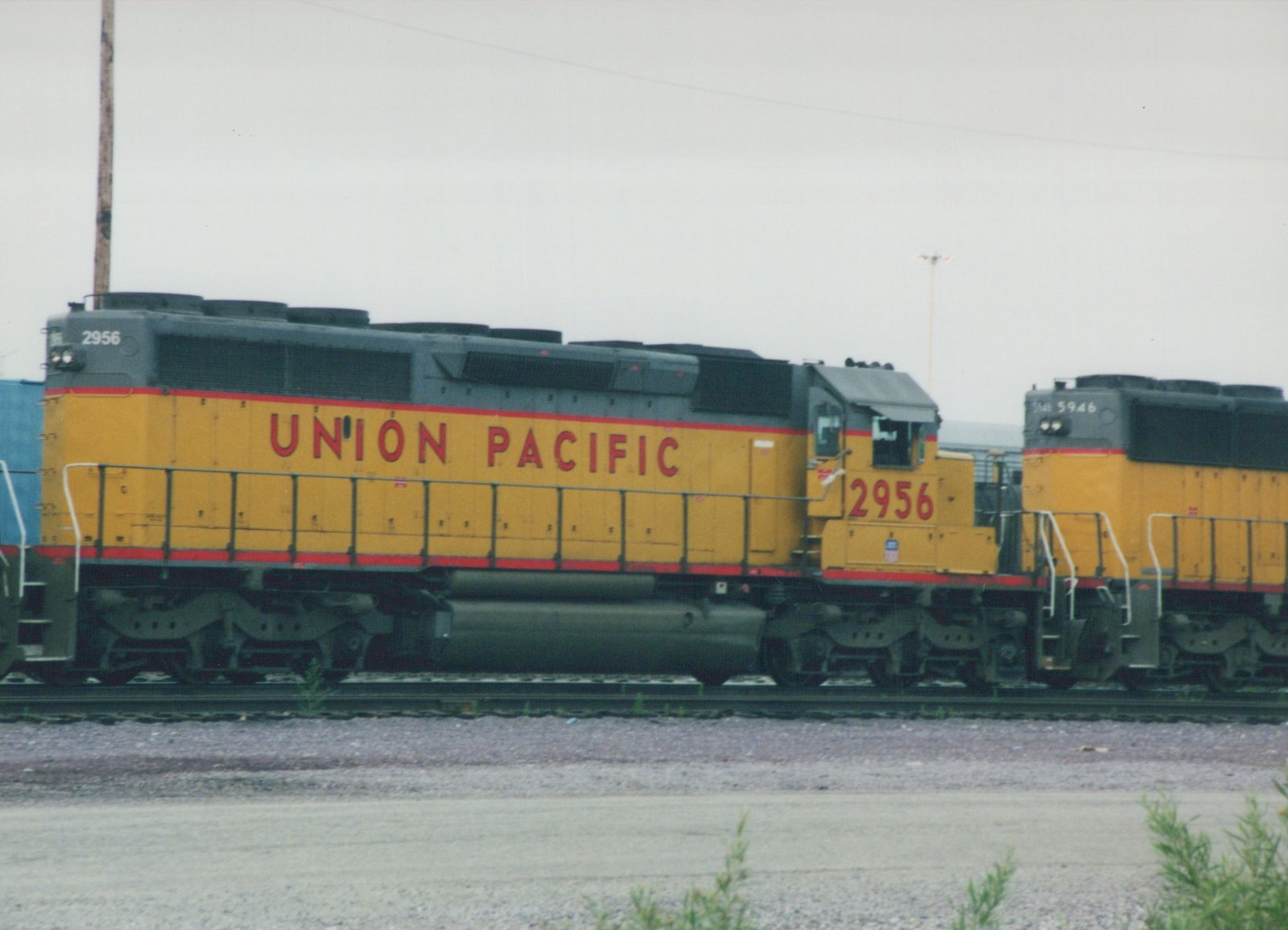 Two yellow and gray Union Pacific diesel locomotives, numbers 2956 and 5946, are parked side by side on railroad tracks in a yard on an overcast day.