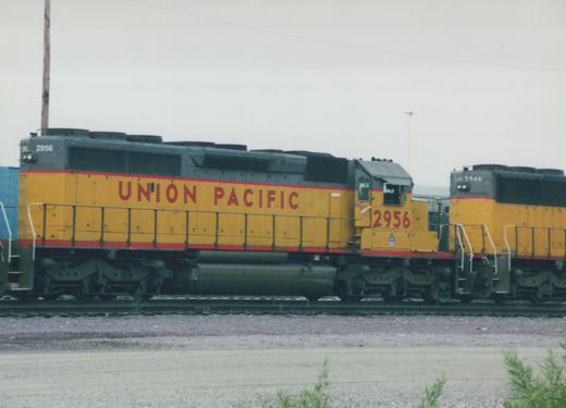 Two yellow and gray Union Pacific diesel locomotives, numbers 2956 and 5946, are parked side by side on railroad tracks in a yard on an overcast day.