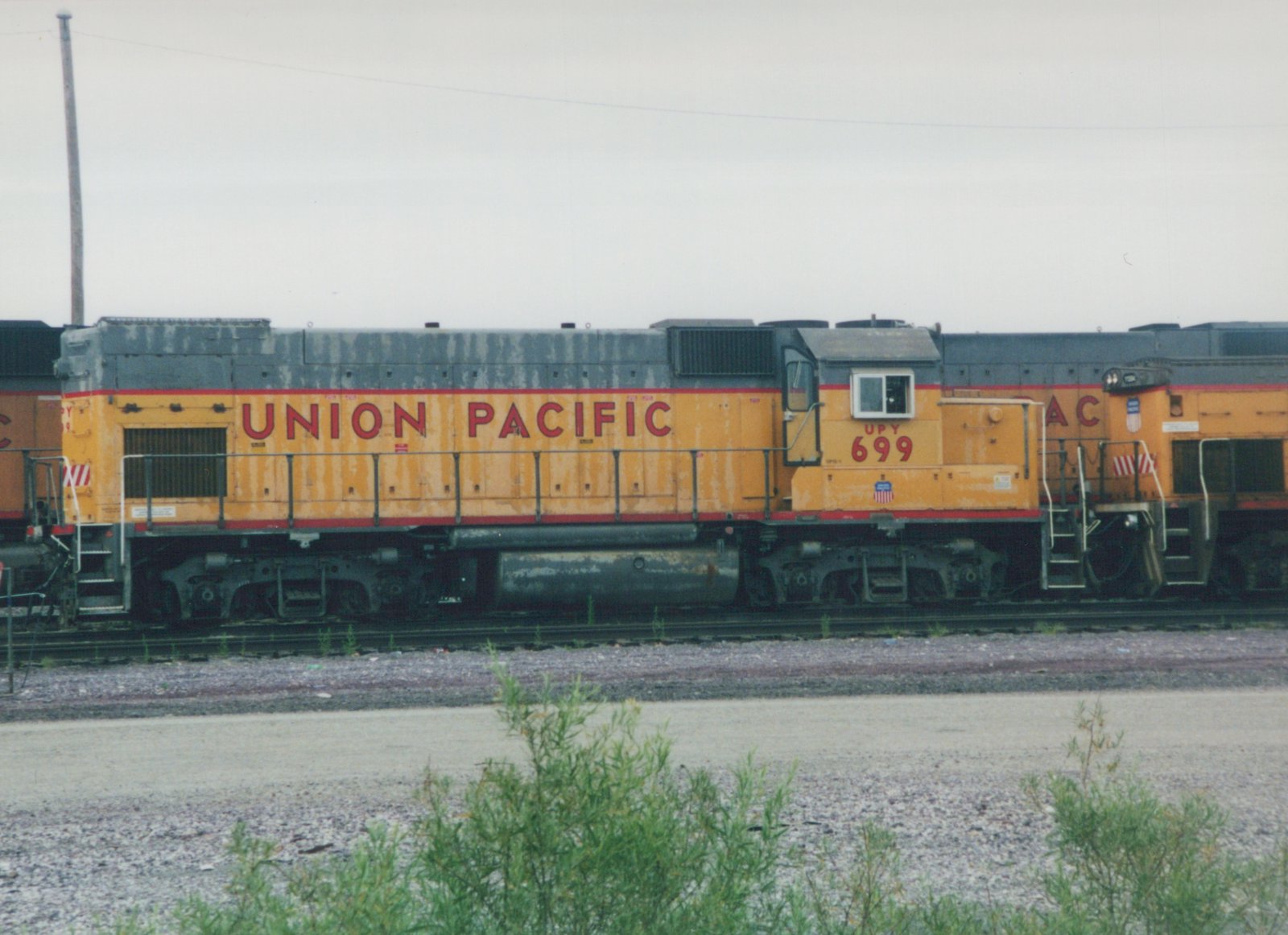 Side view of a yellow and gray Union Pacific diesel locomotive, number 699, sitting on tracks in a gravel yard under an overcast sky.