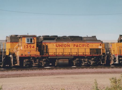 A side view of several yellow and red Union Pacific diesel locomotives, including number 1394, parked on parallel tracks in a gravel yard under a clear blue sky.