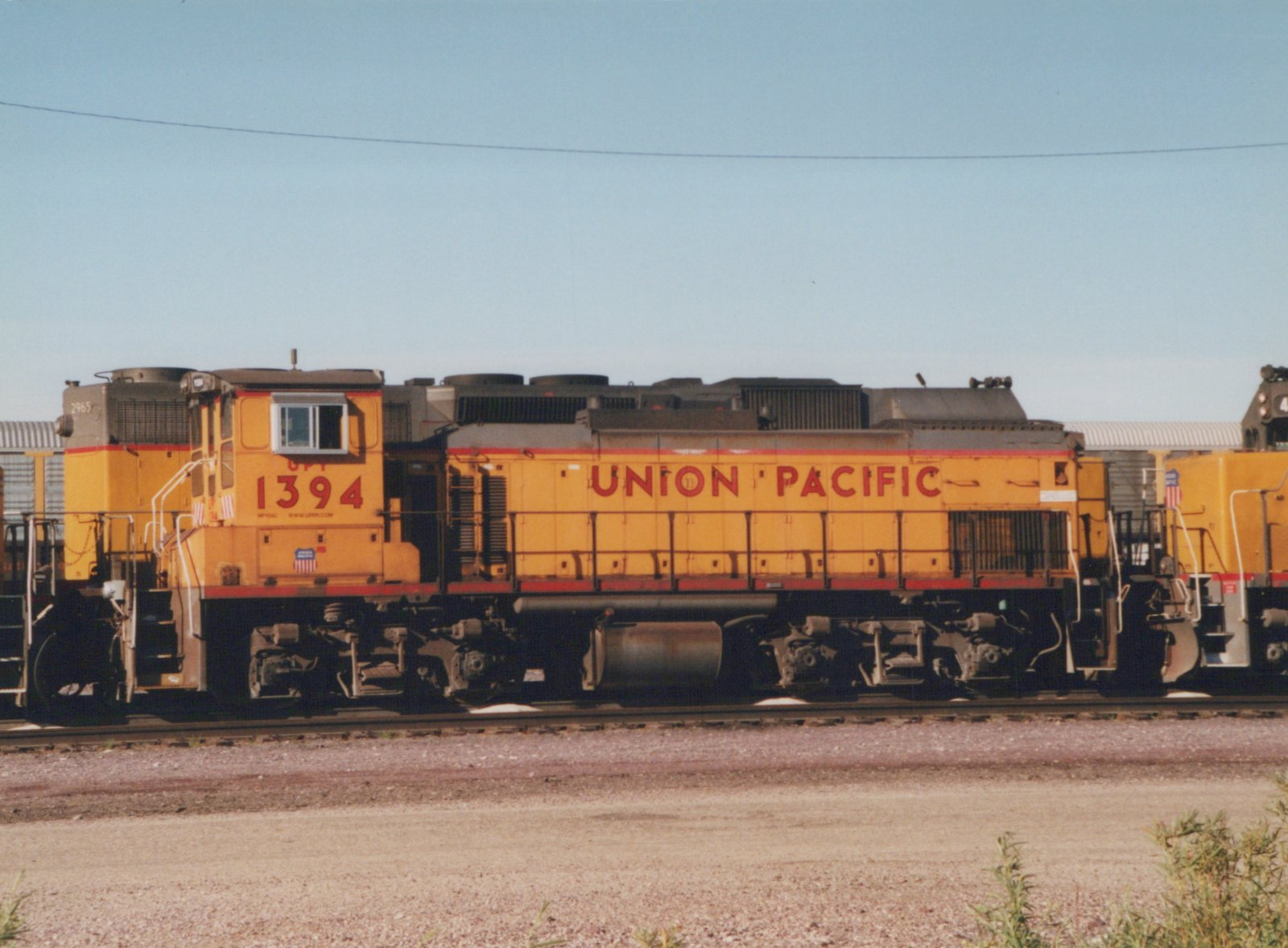 A side view of several yellow and red Union Pacific diesel locomotives, including number 1394, parked on parallel tracks in a gravel yard under a clear blue sky.