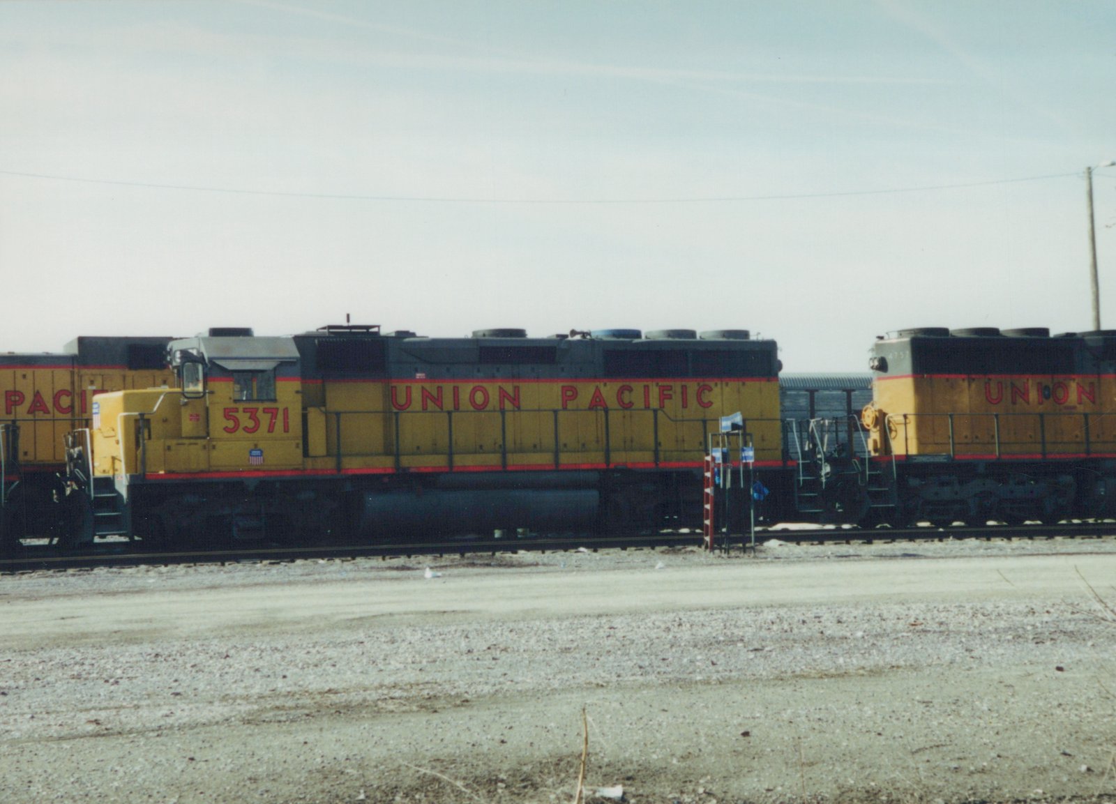 Three Union Pacific diesel locomotives in yellow and grey livery are parked side by side in a gravel yard under a clear sky.