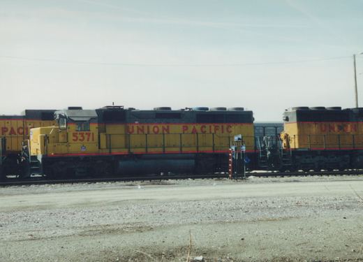 Three Union Pacific diesel locomotives in yellow and grey livery are parked side by side in a gravel yard under a clear sky.