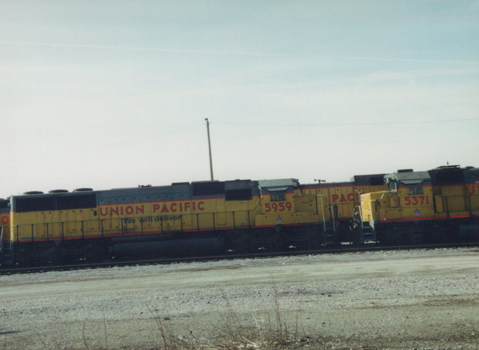 Two yellow Union Pacific diesel locomotives, numbered 5959 and 5371, side by side in a gravel yard under an overcast sky.