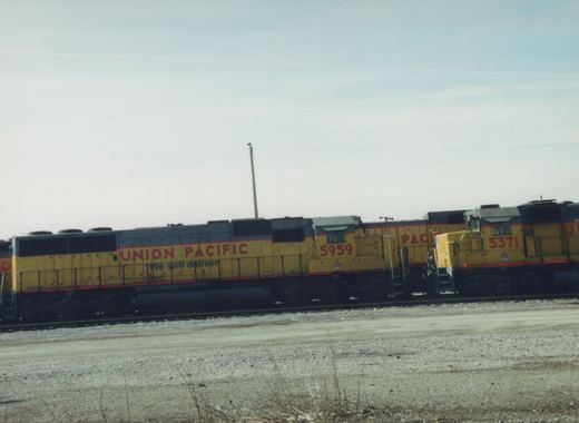 Two yellow Union Pacific diesel locomotives, numbered 5959 and 5371, side by side in a gravel yard under an overcast sky.
