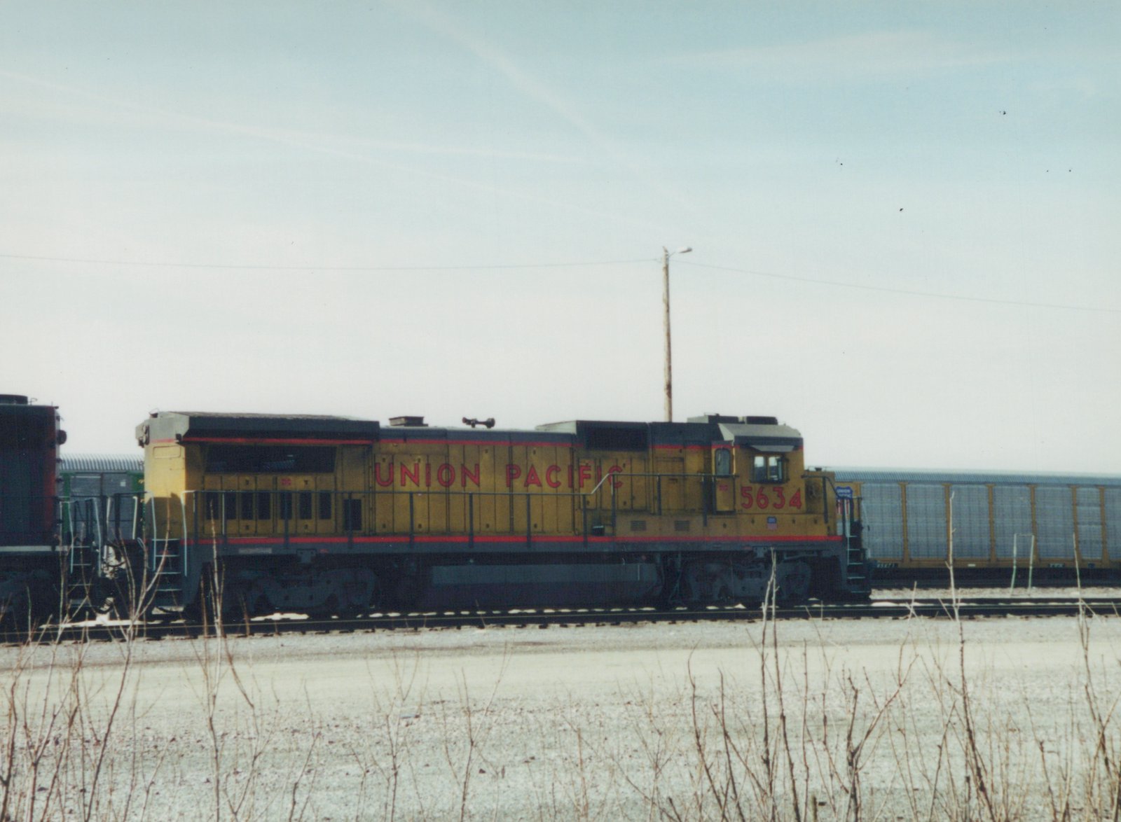 A yellow Union Pacific diesel locomotive, number 5634, stands on a track in a snowy yard, with a freight car behind it.