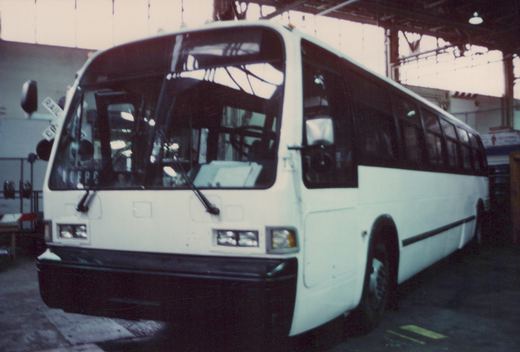 A white motor bus with the number 72 on its side is parked inside a well-lit bus garage, viewed from a three-quarter front angle.