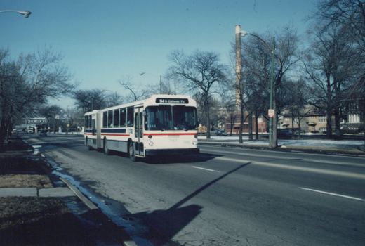 A white, red, and blue articulated bus from the Chicago Transit Authority, labeled with route 94 S. California and fleet number 7157, driving down a tree-lined street with snow on the ground.