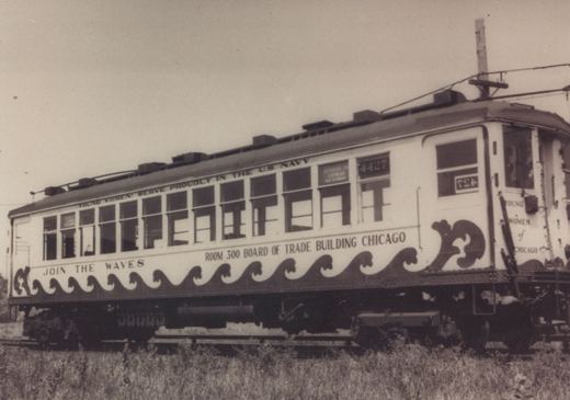 A vintage black and white photo shows a white, wood-bodied electric interurban car numbered 4427 with a navy recruitment ad along its side, sitting on tracks in a grassy area.