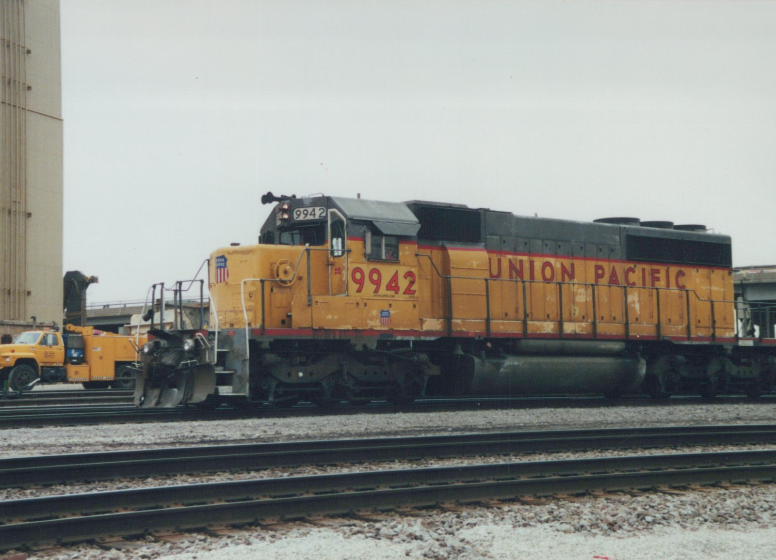 A yellow and red Union Pacific locomotive numbered 9942 is parked on multiple tracks in a rail yard under a gray sky.