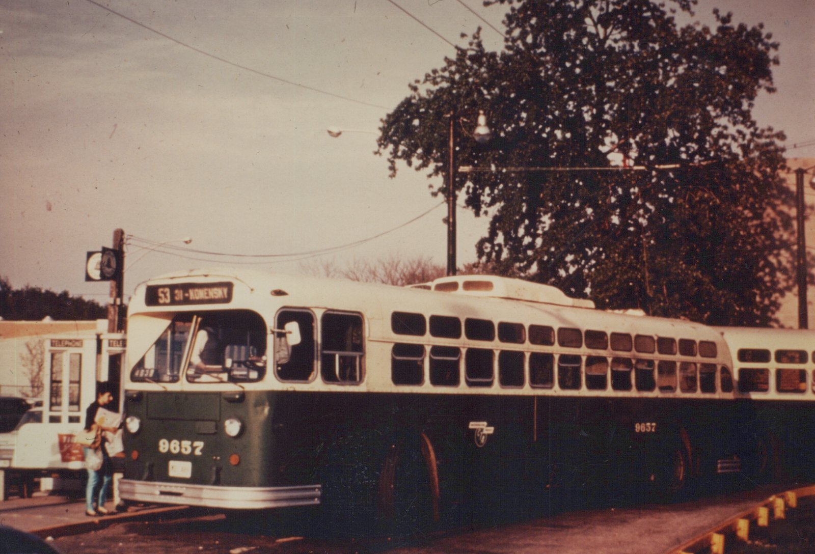 A green and cream Chicago Transit Authority bus, number 9657, is parked on a street corner with people on the sidewalk and a telephone booth in the background.