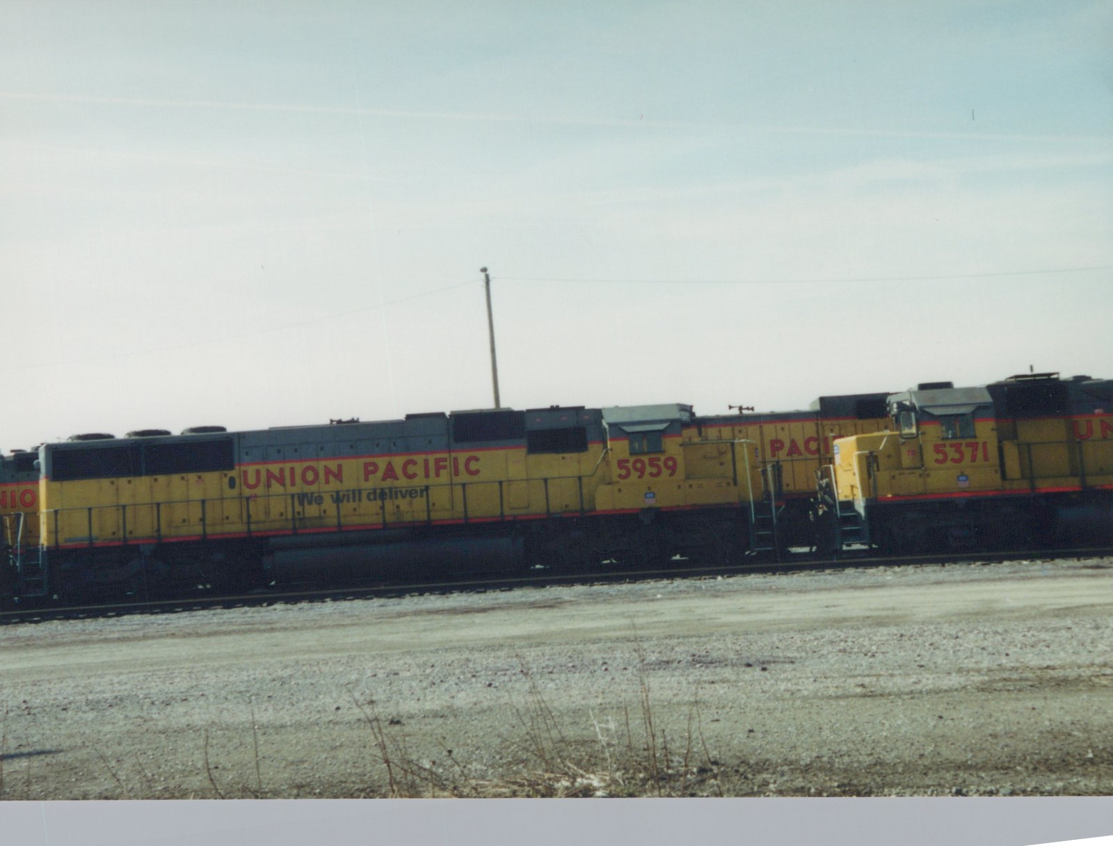 Four yellow and gray Union Pacific diesel locomotives, numbered 5959 and 5371 among others, are parked side by side in a gravel yard under an overcast sky.
