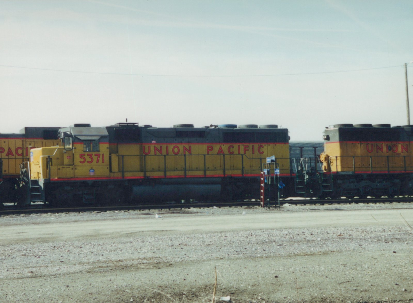Two yellow and gray Union Pacific diesel locomotives, numbers 5371 and 4757, are coupled together on tracks in a gravel yard with snow on the ground under a clear sky.