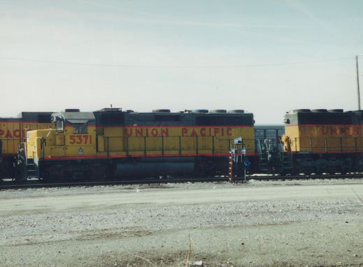 Two yellow and gray Union Pacific diesel locomotives, numbers 5371 and 4757, are coupled together on tracks in a gravel yard with snow on the ground under a clear sky.