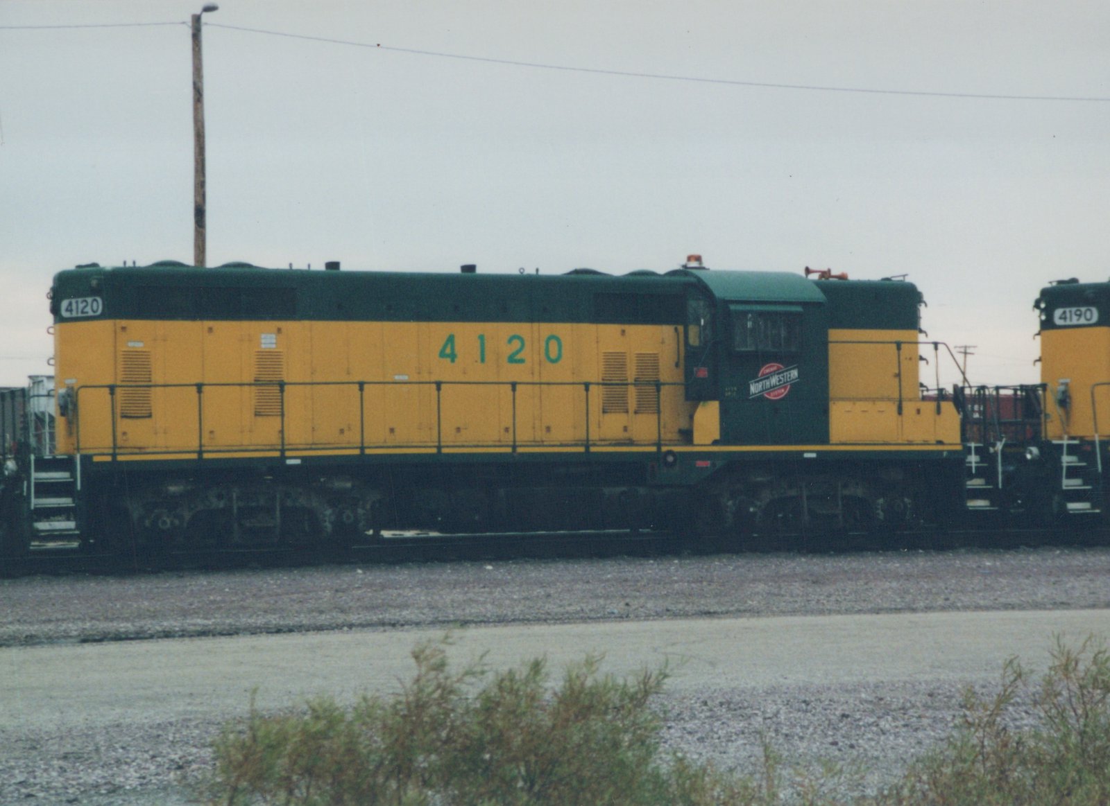 A side view of a Chicago and North Western diesel locomotive, number 4120, painted in yellow and green, standing in a railyard.