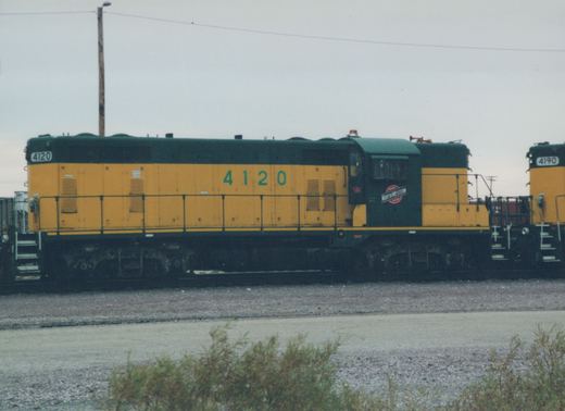 A side view of a Chicago and North Western diesel locomotive, number 4120, painted in yellow and green, standing in a railyard.