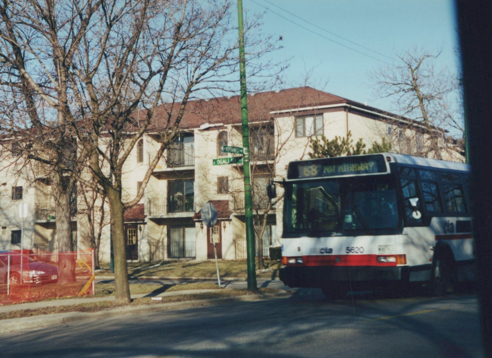 A white and red Chicago Transit Authority bus with the number 5620 on the front is stopped on a street corner with bare trees and an apartment building in the background.