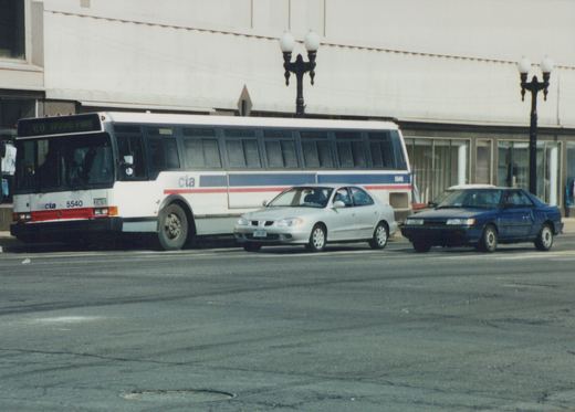 A white, blue and red Chicago Transit Authority bus, number 5540, on route 80 to Irving Park, is parked on a street in Cicero, Illinois, with a silver car and a blue car beside it.
