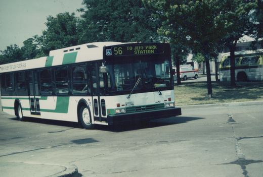 A white and green Pace bus numbered 4882, route 56 to Jefferson Park Station, is parked on a sunny street with trees and another bus in the background.