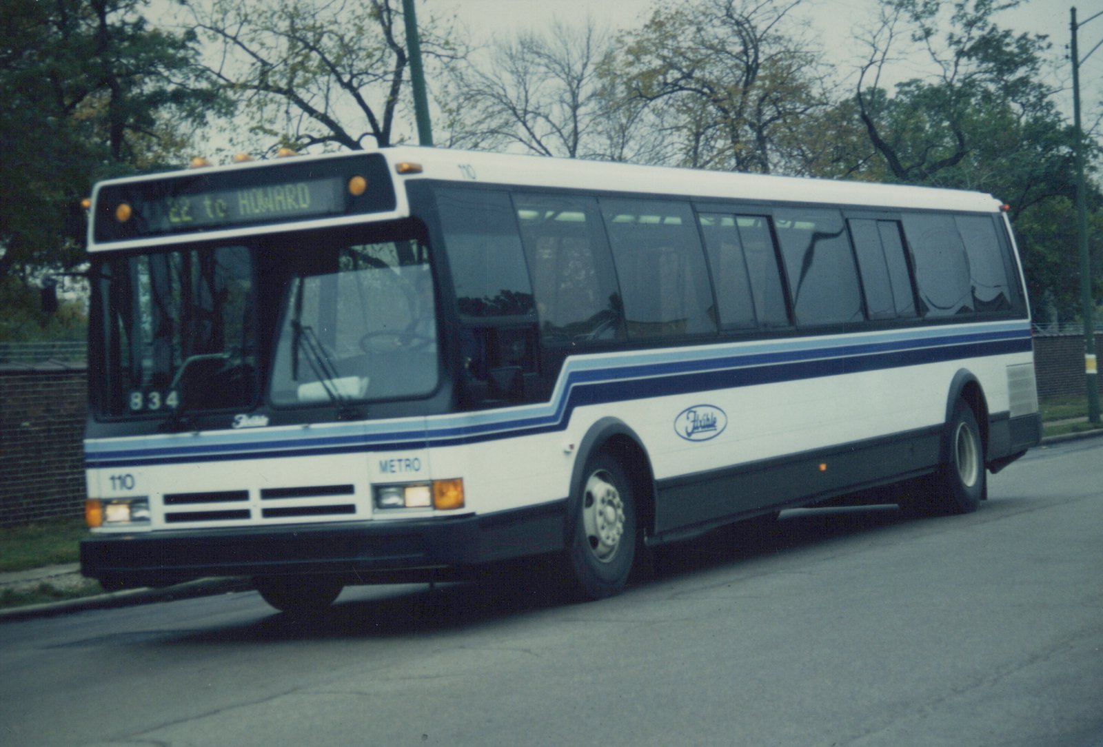 A side-front view of a white and blue RTA bus with the number 110 on the front and side, displaying route 22 to Howard, parked on a street lined with trees.