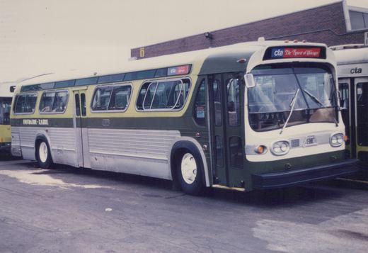 A green, cream, and silver CTA bus with the number P999 parked in a lot, with other buses and a brick building behind it.