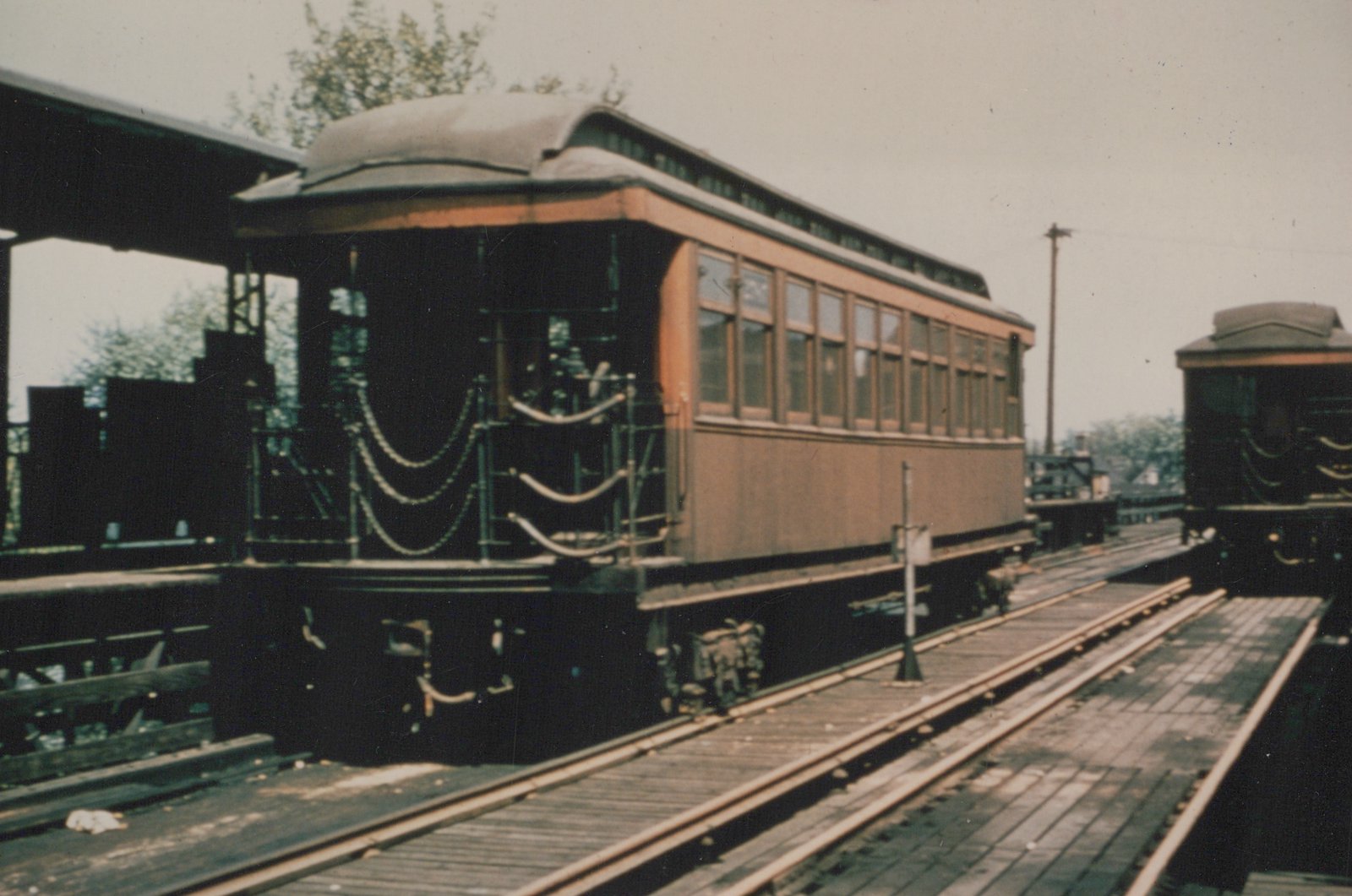 An old photograph of a vintage interurban car on an elevated wooden track platform, showing its rear with decorative festoons and a matching car on a parallel track.