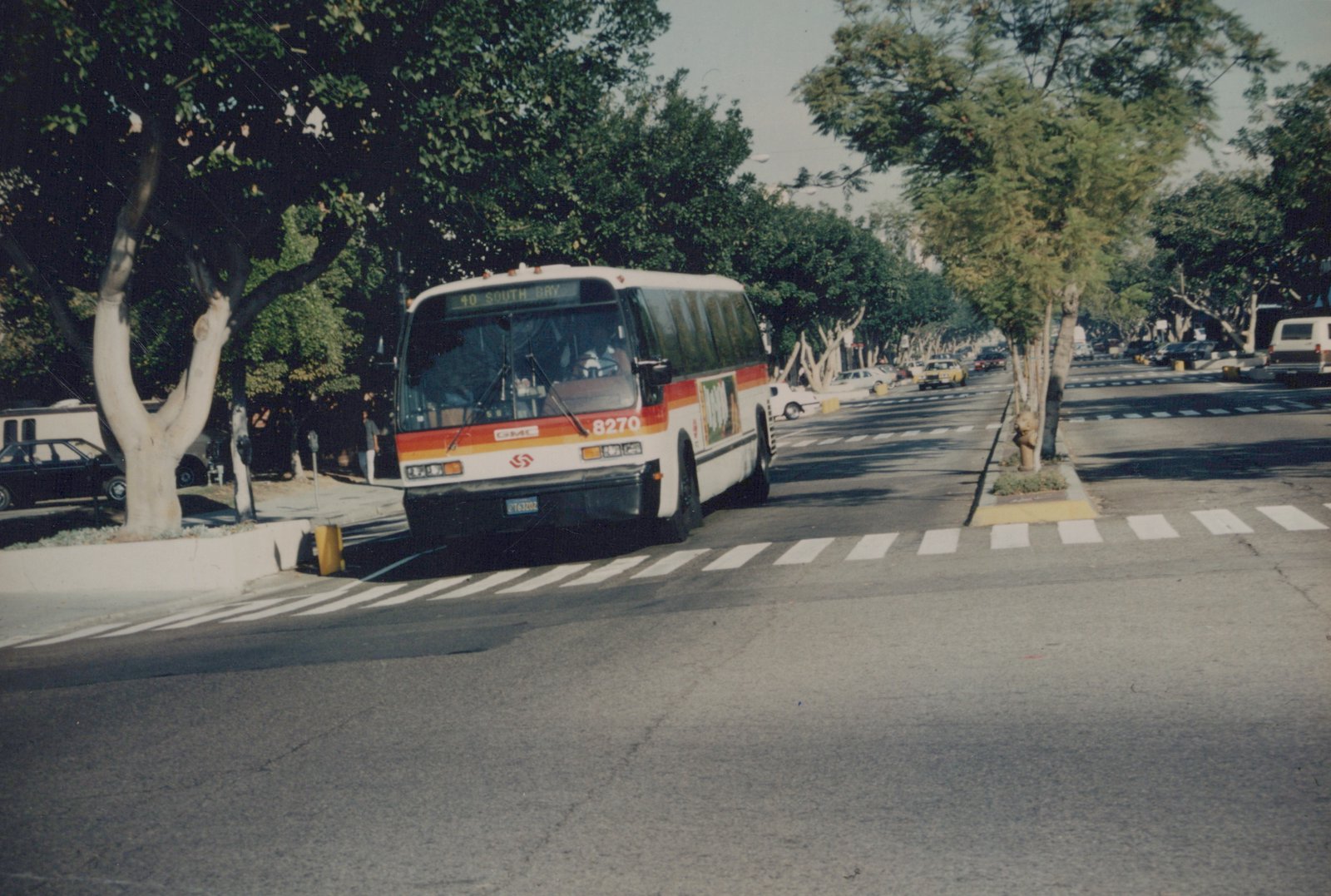 A white and orange GMC bus with the number 8270 on the front, driving down a tree-lined street with a destination sign reading '40 SOUTH BAY'.
